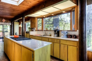 Una cocina con armarios de madera, una isla grande, una cafetera y un ventanal con vistas a árboles.