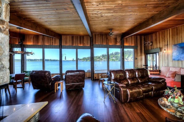 A spacious living area with a large window overlooking a body of water, wooden walls, and leather furniture.