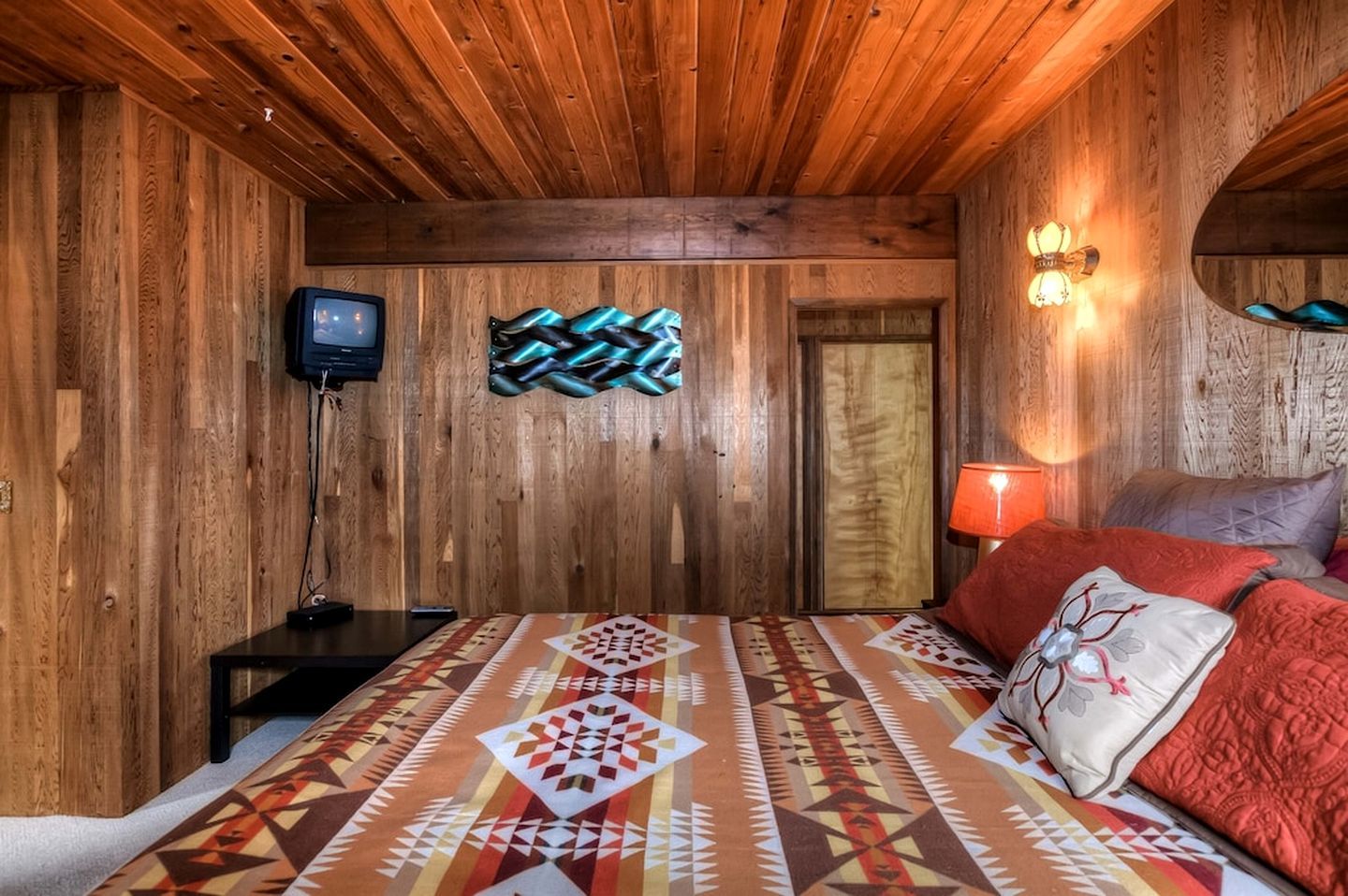 Una habitación de madera con una cama, un televisor y una lámpara de pared.