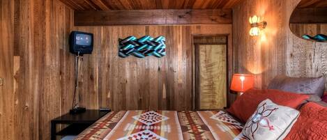 Una habitación de madera con una cama, un televisor y una lámpara de pared.
