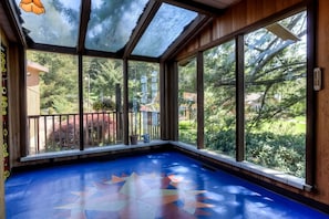 Ein Wintergarten mit großen Fenstern, einem blauen Boden mit geometrischem Muster und einer Holzbalkendecke.