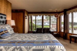 A bedroom with a large bed, a view of a dock and water, and a window with decorative curtains.