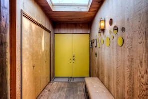 Un pasillo con paredes de madera, una puerta amarilla, un banco y un tragaluz.