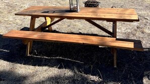 A picnic table with a lantern and a fire pit in a natural setting with mountains in the background.