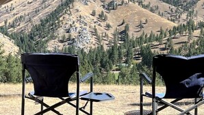 A tent with two chairs and a small table, set against a mountainous backdrop.