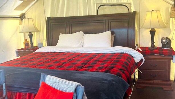 A bed with a red and black checkered bedspread, two white pillows, and a wooden headboard. There are two bedside tables with lamps and a small decorative item on one.