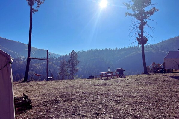 A campsite with tents, a picnic table, and a clear view of a forested mountain range.