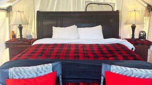 A tented room with a bed, two bedside tables with lamps, and a window with curtains.