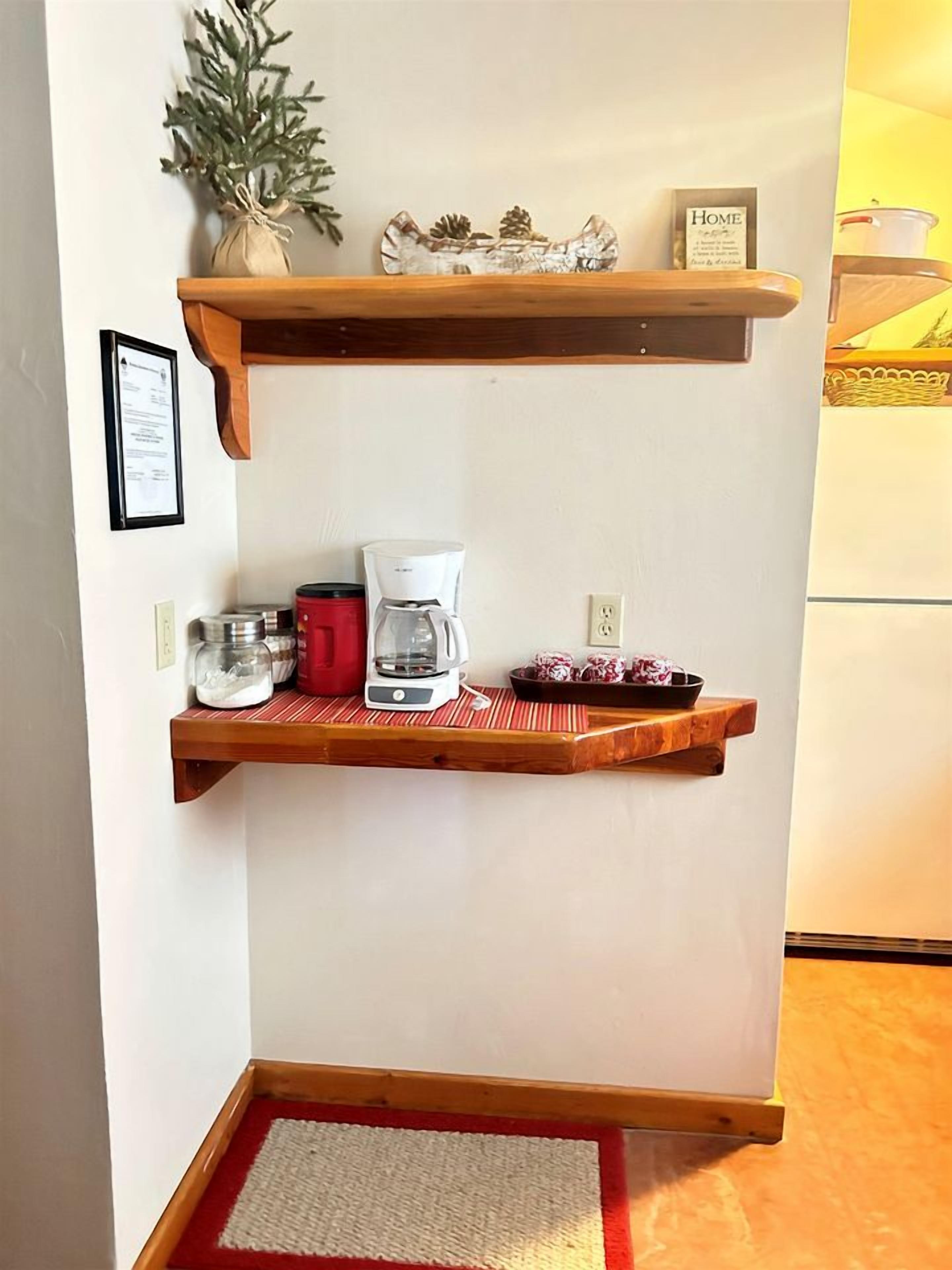 A kitchen with wooden shelves, a coffee maker, jars, and a bowl of cookies.