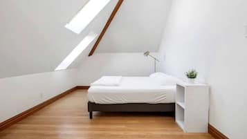 A modern, minimalistic bedroom with a sloped ceiling, a bed, a bedside table with a lamp, and a small plant.
