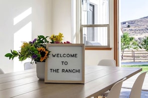 A welcome sign with a floral arrangement on a wooden table in a room with a view of a hilly landscape. - Breathtaking Cottage with Hot-tub in Eagle Mountain, Utah (Eagle Mountain)