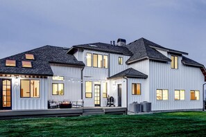 Una casa grande y moderna de dos pisos, con un porche cubierto y varias ventanas.