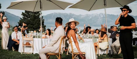 A wedding reception with guests seated at tables under large umbrellas, with a mountainous backdrop.
