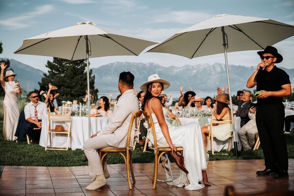 A wedding reception with guests seated at tables under large umbrellas, with a mountainous backdrop.