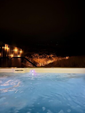 Ein Schwimmbad bei Nacht mit einer Holzkonstruktion und warmer Beleuchtung.