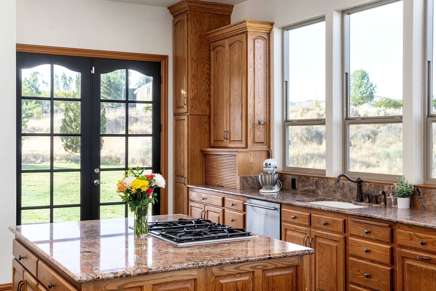 Una cocina con encimeras de granito, armarios de madera, estufa a gas y vistas al exterior a través de grandes ventanales.