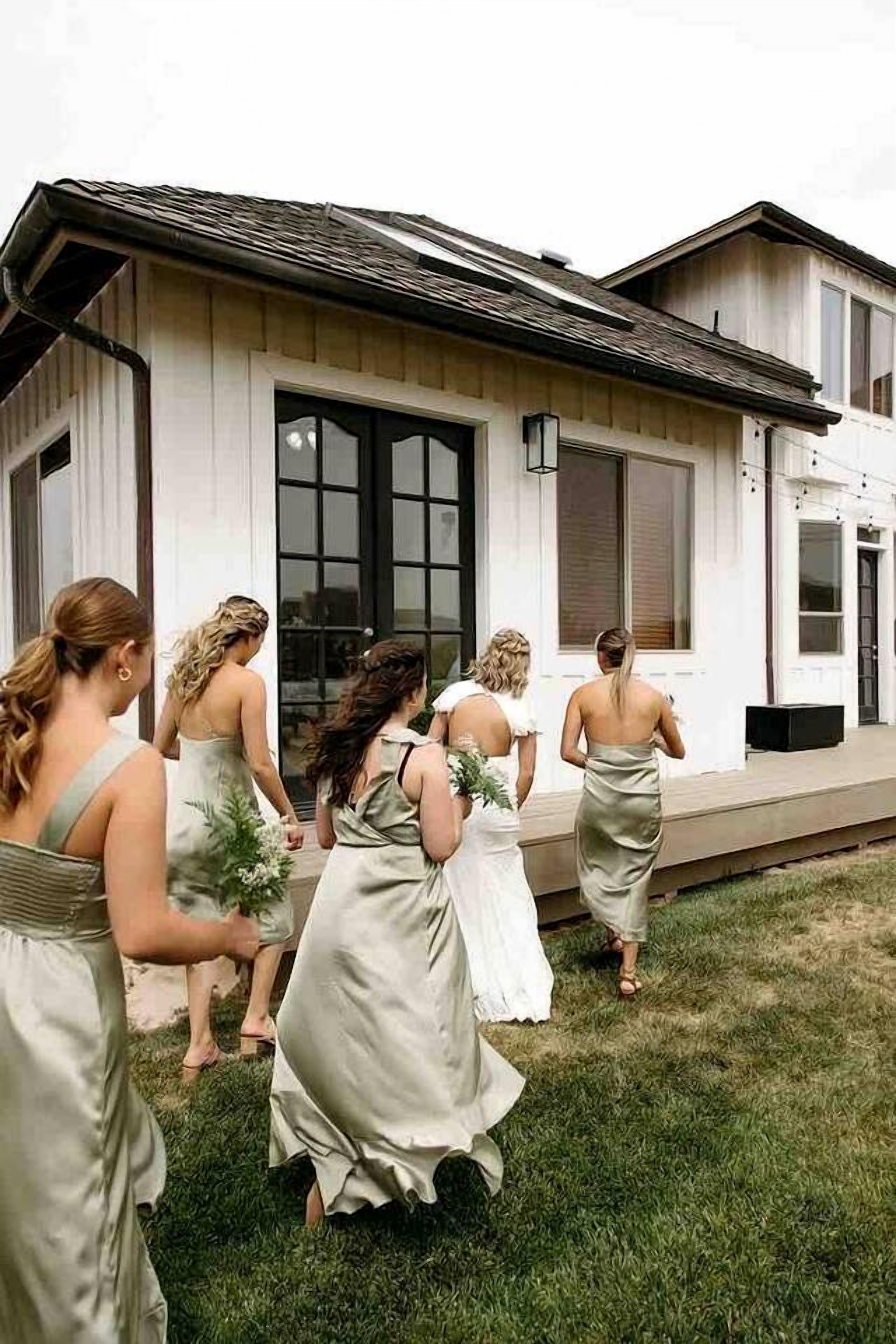 Un groupe de femmes, vêtues de robes élégantes, se dirige vers un bâtiment blanc doté de grandes fenêtres et d’un porche.