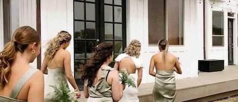 A group of women in formal dresses walking towards a white building with large windows and a porch.