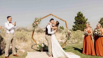 A wedding ceremony outdoors with a wooden arch and floral arrangements.