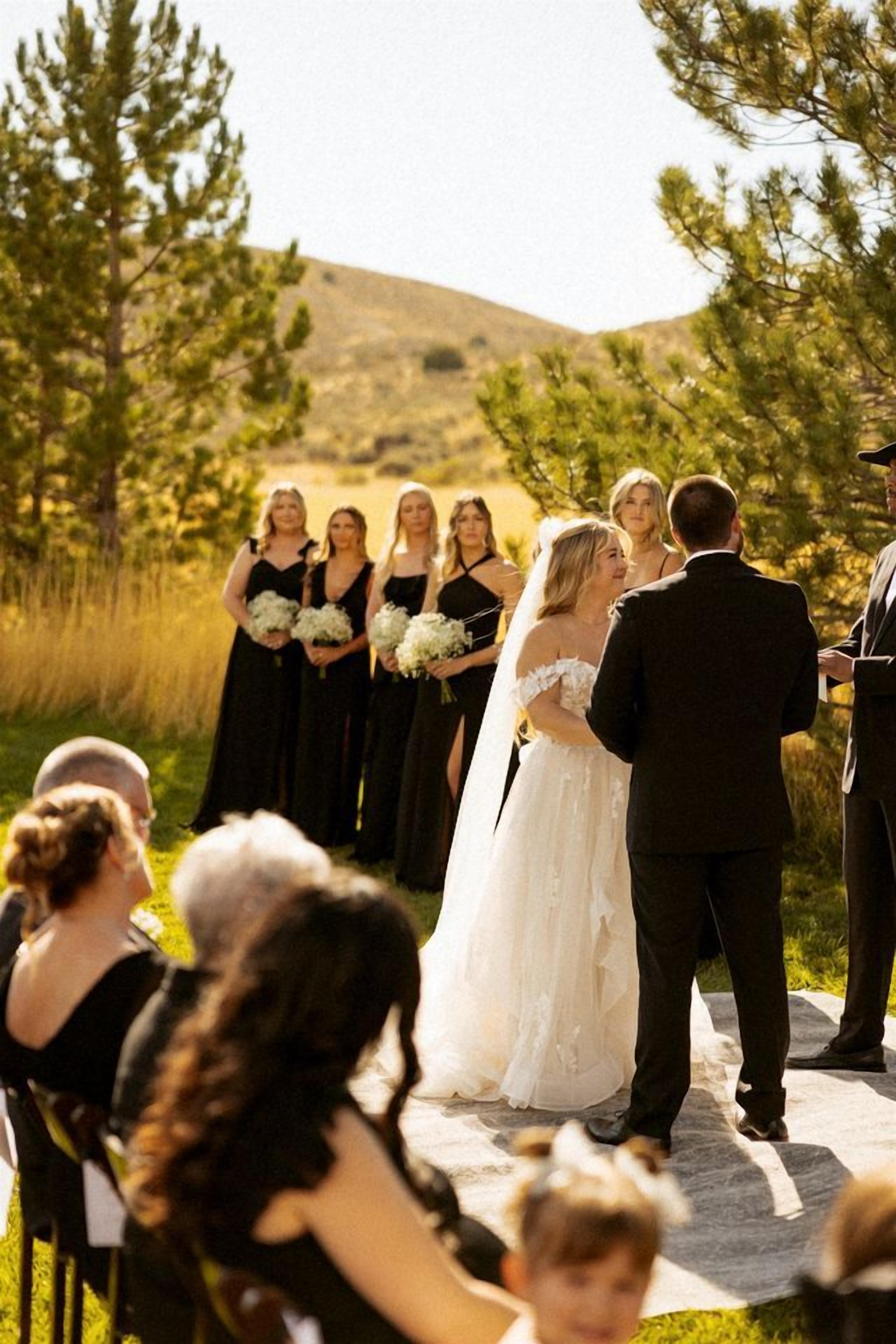 A wedding ceremony outdoors with a clear sky and a hilly landscape in the background.