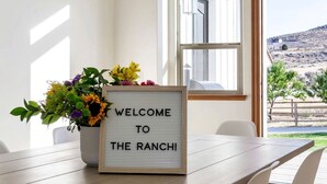 A welcome sign with a floral arrangement on a wooden table in a room with a view of a hilly landscape. - Breathtaking Cottage with Hot-tub in Eagle Mountain, Utah (Eagle Mountain)