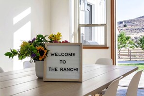 A welcome sign with a floral arrangement on a wooden table in a room with a view of a hilly landscape.