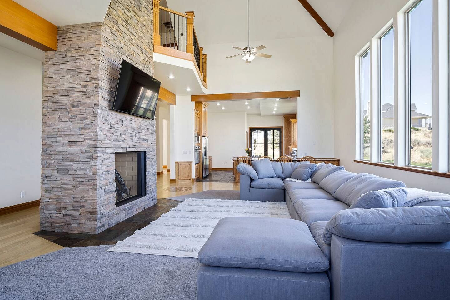 A spacious living room with a stone fireplace, a large sectional sofa, and a dining area with wooden cabinets.