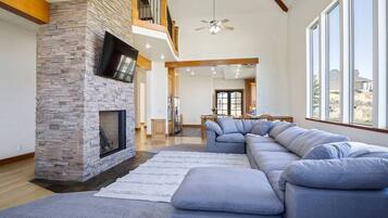 A spacious living room with a stone fireplace, a large sectional sofa, and a dining area with wooden cabinets.