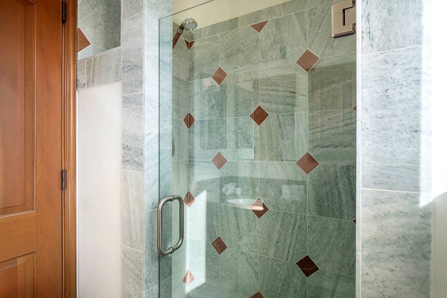 Eine Dusche mit Glastür und Handlauf, gefliest mit einem geometrischen Muster.