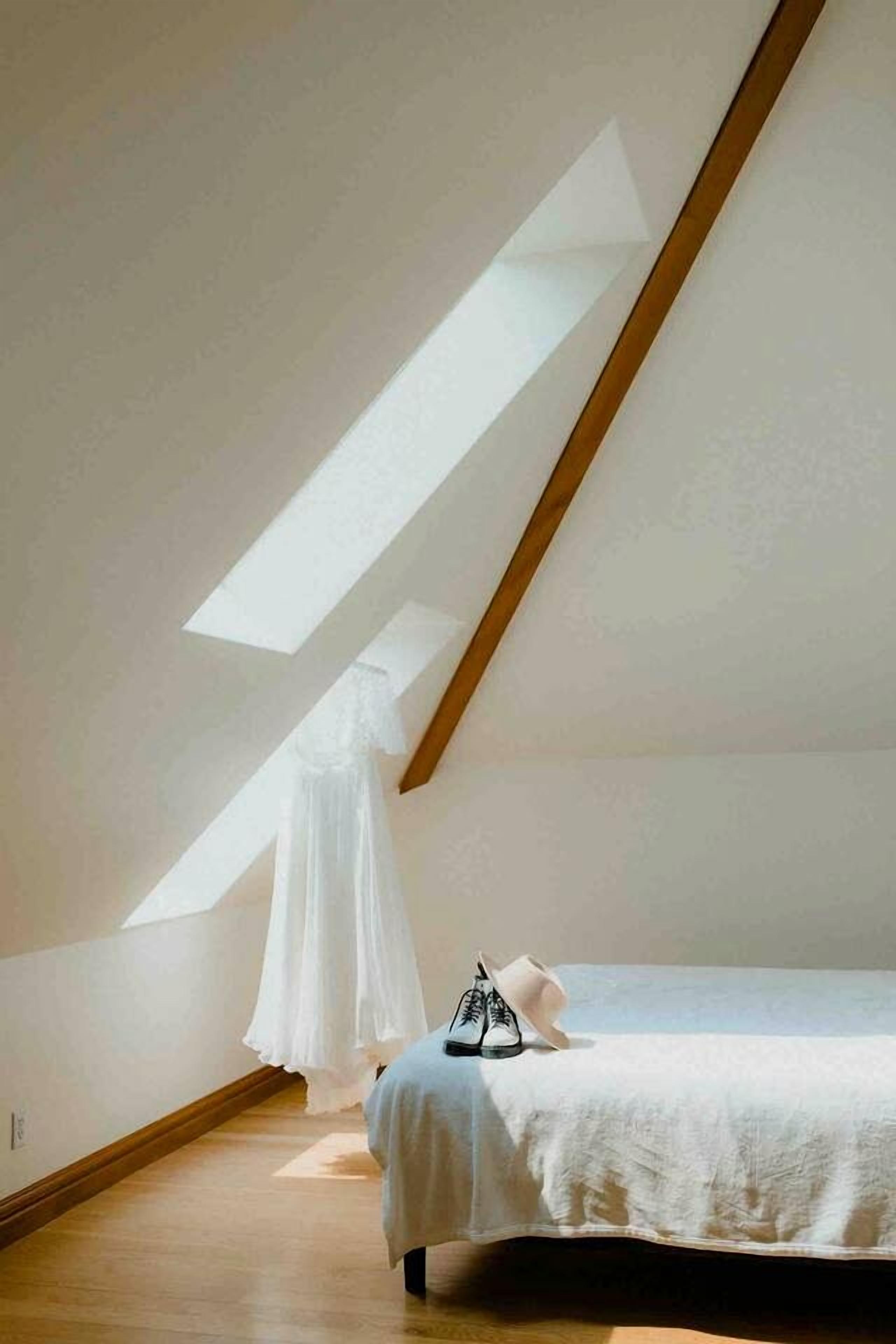 Un dormitorio con techo inclinado, una cama con colcha blanca, un dosel blanco y un par de zapatos en el suelo.