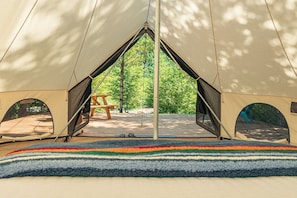 A tent with a central entrance, a picnic table, and a view of a forest.