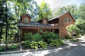A two-story wooden house with a covered porch, surrounded by lush greenery. - Beautiful Cabin with Hot Tub Surrounded by Trees in Confluence, Pennsylvania (Confluence)
