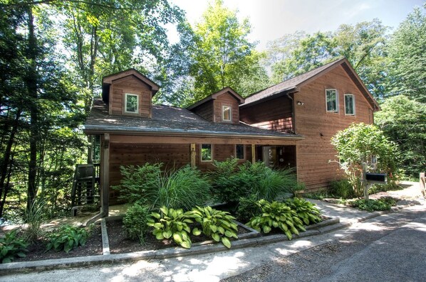 A two-story wooden house with a covered porch, surrounded by lush greenery.