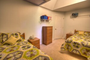 A bedroom with two beds, a dresser, a door, and a shelf with storage boxes.
