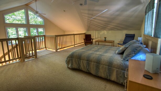 A bedroom with a large bed, a desk, a chair, a window, and a balcony. - Beautiful Cabin with Hot Tub Surrounded by Trees in Confluence, Pennsylvania (Confluence)