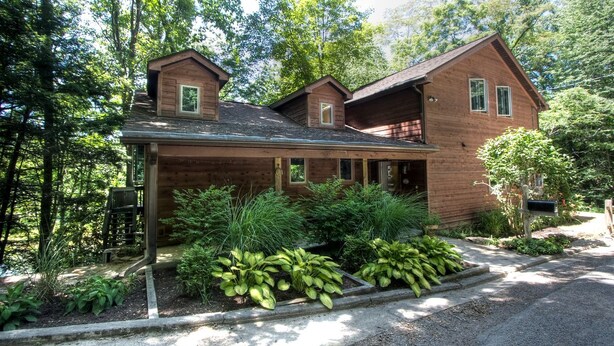 A two-story wooden house with a covered porch, surrounded by lush greenery. - Beautiful Cabin with Hot Tub Surrounded by Trees in Confluence, Pennsylvania (Confluence)