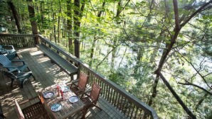 A deck with wooden furniture and a table set for dining, surrounded by dense forest. - Beautiful Cabin with Hot Tub Surrounded by Trees in Confluence, Pennsylvania (Confluence)