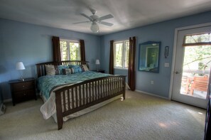A bedroom with a bed, two nightstands, a ceiling fan, and a door leading to an outdoor area.