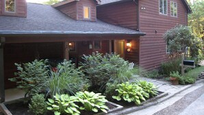 A two-story wooden house with a covered porch, a small attached garage, and a well-maintained garden with various plants. - Beautiful Cabin with Hot Tub Surrounded by Trees in Confluence, Pennsylvania (Confluence)