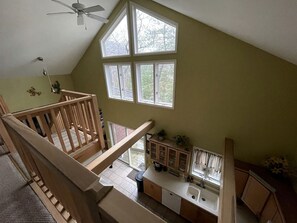A multi-level interior with a kitchen area, wooden staircase, and large windows.