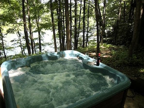 A hot tub in a forested area with trees and a body of water in the background.