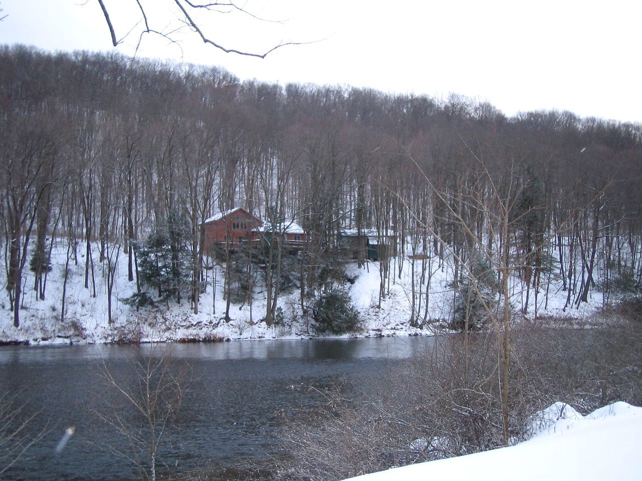 A cabin by a lake surrounded by snow-covered trees.
