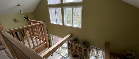 Ein mehrstöckiger Innenraum mit Küchenbereich, einer Holztreppe und großen Fenstern.