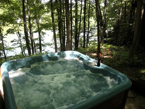 A hot tub in a forested area with trees and a body of water in the background.
