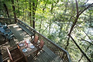 A deck with wooden furniture and a table set for dining, surrounded by dense forest.