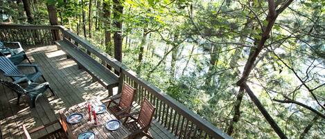 Una terraza con muebles de madera y una mesa lista para comer, rodeada de un bosque frondoso.