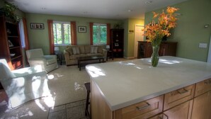 A spacious living room with a large sofa, a coffee table, and a dining area with a white island. - Beautiful Cabin with Hot Tub Surrounded by Trees in Confluence, Pennsylvania (Confluence)