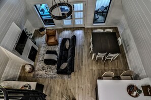 A high-ceilinged room with a black sofa, white chairs, a dining table, and a skylight.