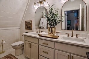 A bathroom with a white vanity, gold fixtures, a potted plant, and a large mirror.