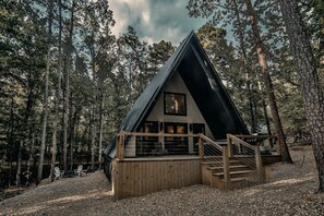 A cabin with a sloped roof, wooden deck, and a large window.